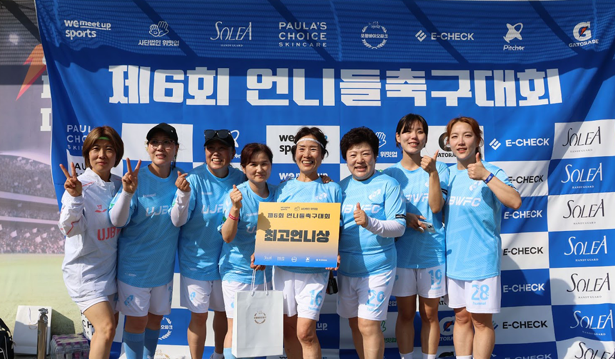 하늘색 유니폼을 입고 있는 최고언니상 수상 팀. 언니들축구대회 현수막 앞에서 브이, 하트, 엄지 등의 포즈를 취하며 정면을 바라보고 있는 우승 팀원들.